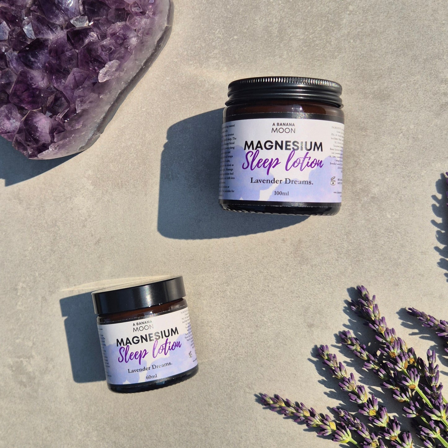 Two jars of magnesium sleep lotion with lavender flowers and an amethyst crystal on a light surface.